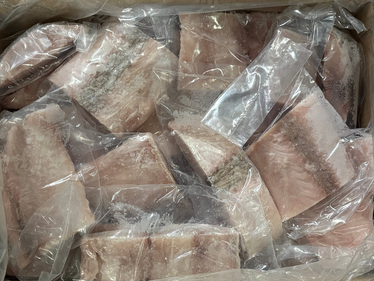 Frozen fish fillets in clear plastic bags, stacked inside a cardboard container.