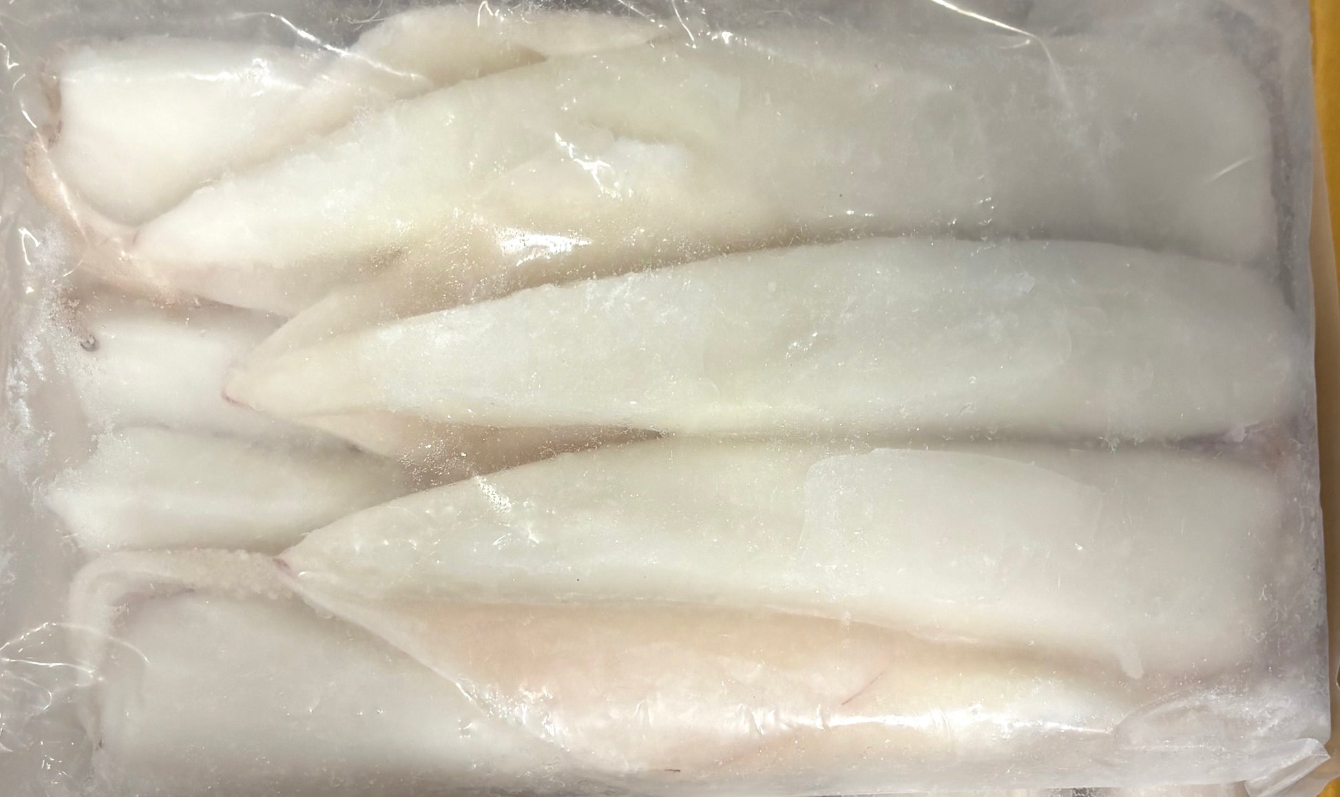 Frozen squid sealed in clear plastic packaging, showing a smooth white surface with light frosty texture.